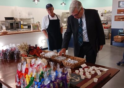 Senator Sheldon Whitehouse stands in from to a table full of colorfully packaged toffee. He is holding a package in his hand and reading the label.